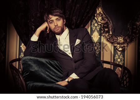 Handsome man in elegant black suit posing in the classical vintage interior.