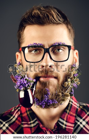 Handsome young man in glasses and a beard of flowers smoking a pipe.