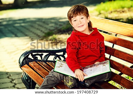 Happy boy sitting on the bench and reading a book. Summer day.
