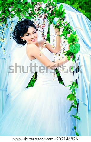 Beautiful elegant asian bride stands under the wedding arch. Wedding dress and accessories. Wedding decoration.