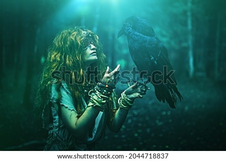 Halloween. A fairytale forest witch with a mask covering her eyes talks to a black raven, standing in the thicket of the forest. Mystical ritual of death. Woman shaman in ritual garment. Stock fotó © 