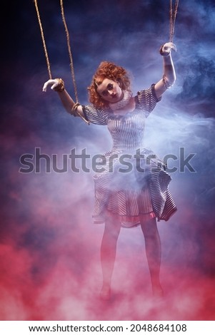 Puppet theater and circus. Portrait of an actress dressed in vintage style playing a role of a doll on strings at a puppet theater performance. Full length portrait with magic red and blue smoke.