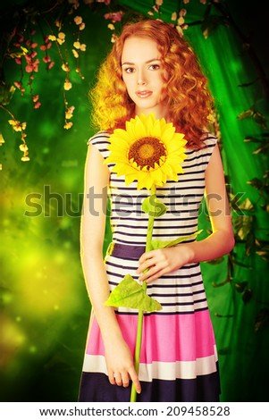 Beautiful red-haired girl with sunflower smiling at camera. Summer.