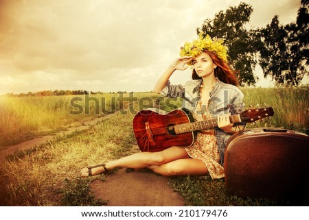 Romantic girl in a wreath of wild flowers travelling with her guitar. Summer. Hippie style.