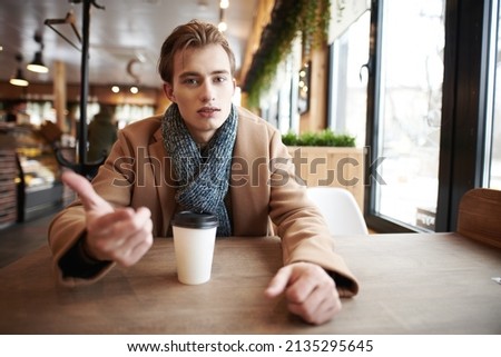 A modern handsome young man in stylish winter clothes drinks hot coffee sitting at a table in a cozy caf? on a cold winter day and talk to someone opposite him. People, communication and lifestyle. Photo stock © 