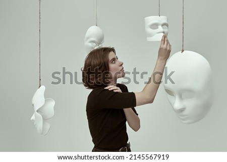 Human roles. A girl in black clothes stands in a white room among different masks deciding which one to choose. Hypocrisy. Mental disorders. Photo stock © 