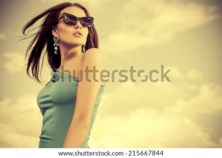 Portrait of a charming lady in beautiful elegant dress and sunglasses against the sky.