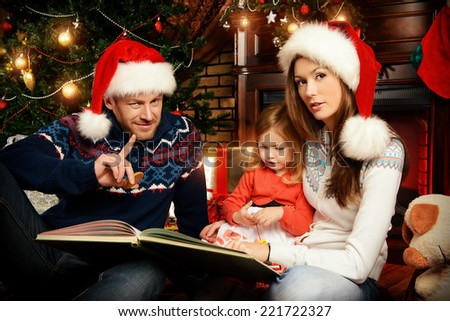 Happy family reading fairy tales at home by the fireplace and the Christmas tree.