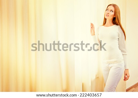 Beautiful young woman standing at the window in the room.