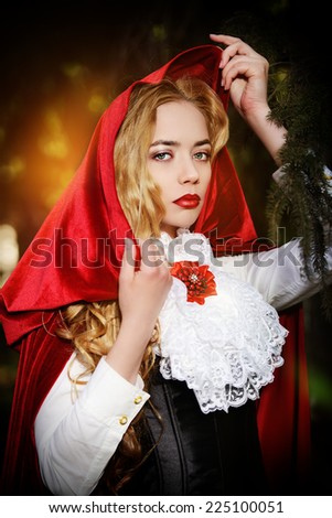 Portrait of a stunning blonde lady in  old-fashioned dress and red cloak in a fairy forest.