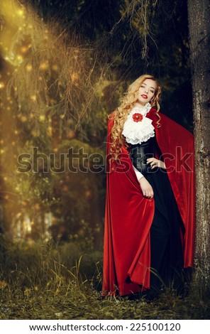 Beautiful blonde woman in  old-fashioned dress and red cloak in a fairy forest.