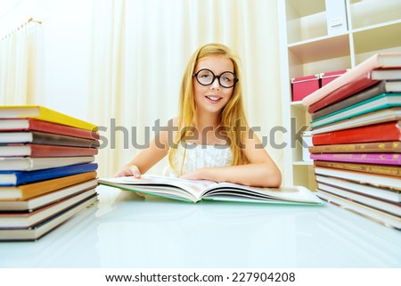 Teen girl sitting at table at home with piles of books and smiles. Educational concept.