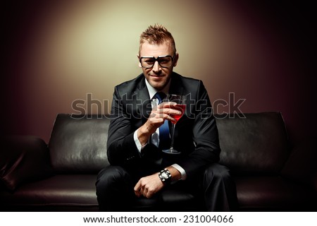 Portrait of a handsome mature man in elegant suit drinking red wine. He is sitting on a leather couch in a luxurious interior.