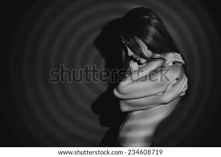 Black-and-white portrait of a sensual naked woman posing over black background. Play of light and shadows.