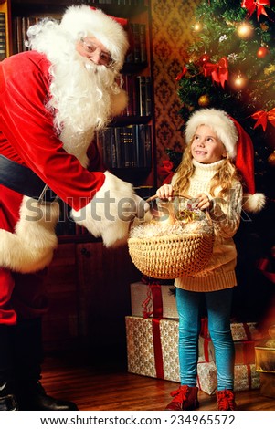 Happy little girl sitting with Santa Claus and rejoice a gift. Christmas decoration.