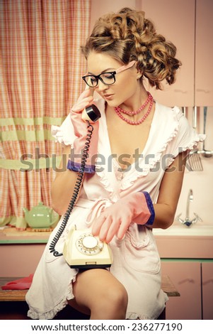 Beautiful sexy pin-up girl talking on the phone on a pink kitchen. Fashion.