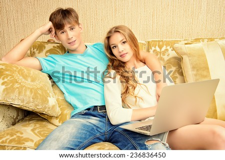 Happy young couple websurfing on internet with laptop. They sit in the cozy living room of their home.