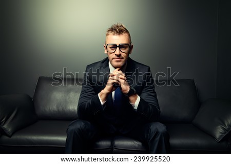 Portrait of a handsome mature man in elegant suit sitting on a leather couch in a luxurious interior.