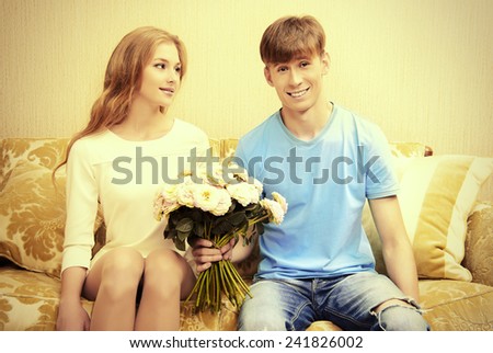 Young man giving flowers to his sweetheart. They are in the cozy living room. Family, love concept.