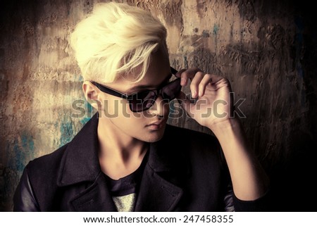 Portrait of a handsome male model with blond hair wearing black jacket and sunglasses. Urban style. Fashion.