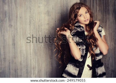 Fashion shot of a pretty teenager girl with beautiful long curly hair wearing white knitted dress and fur jacket. Beauty, fashion.