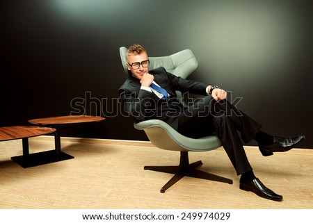 Imposing mature man in elegant suit sitting on a leather chair in a modern luxurious interior. Fashion. Business.