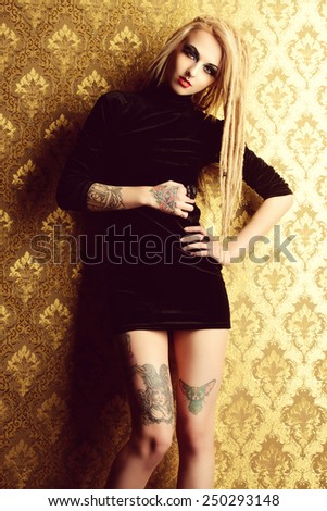 Attractive sexy girl with black make-up and long dreadlocks standing by the vintage wall. Gothic woman. Fashion. Cosmetics, hairstyle. Tattoo.