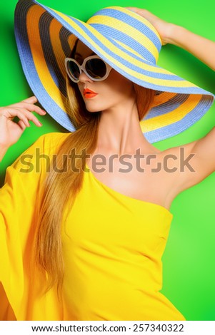 Beautiful fashionable lady wearing bright yellow dress over green background. Beauty, fashion concept. Optics. Summer vacation.
