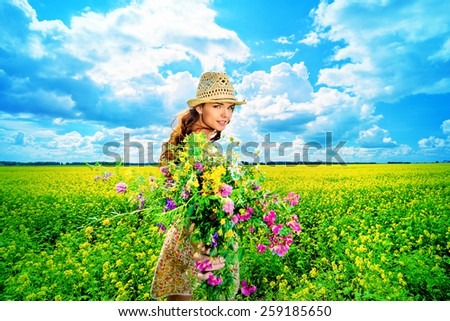 Happy young woman standing in a field of blooming yellow flowers. Summer.
