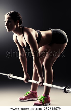 Strong young woman with beautiful athletic body doing exercises with barbell. Fitness, bodybuilding. Health care.