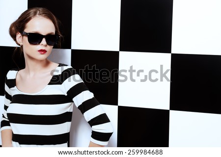 Beautiful fashion model posing in dress in black and white stripes on a background of black and white squares. Beauty, fashion concept. Business style.