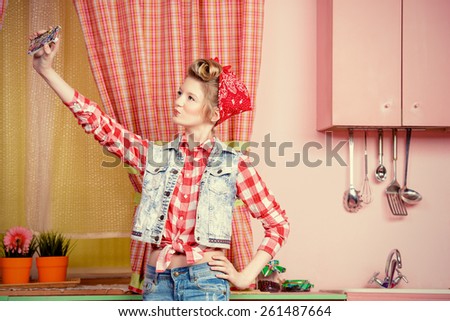 Pretty pin-up girl teenager taking picture of herself on a pink kitchen. Beauty, youth fashion. Pin-up style. Selfie.
