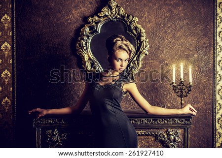Elegant young woman in black evening dress posing in vintage interior. Fashion shot.
