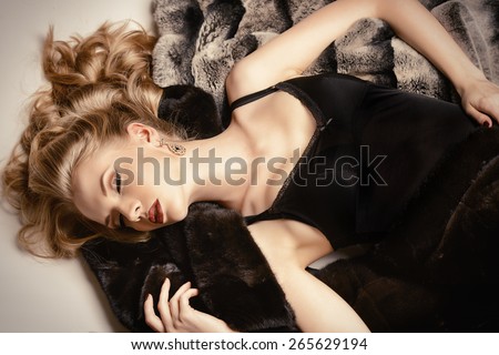 Stunning young woman with beautiful blonde hair lying on furs. Luxury, rich lifestyle. Jewellery. Fashion shot.