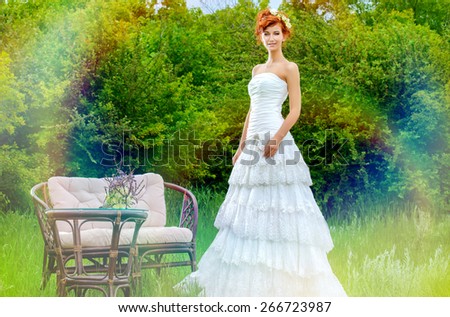 Lovely elegant red-haired bride stands on the lawn. Wedding dress and accessories.