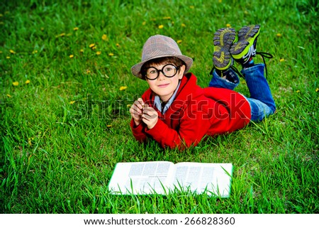 Cute 7 years old boy lying on a grass and reading a book. Summer day.
