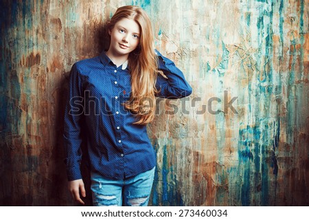 Portrait of a cute smiling teen girl standing by the grunge wall.