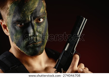 Close-up portrait of a brave soldier in war paint holding a gun. Black background. Military, war. Special forces.