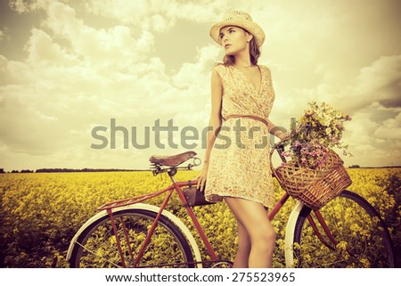 Romantic young woman stands in a field with her bicycle and a basket with wild flowers. Summer.