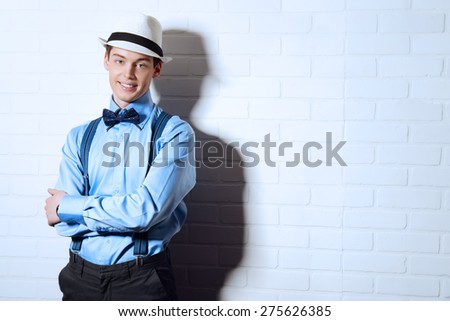 Romantic young man stands by the brick wall and smiling to camera. Men\'s beauty, fashion.