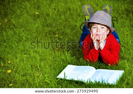 Cute 7 years old boy lying on a grass with a book. Summer day.