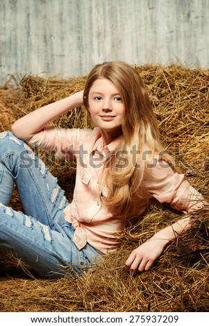 Pretty girl teenager in shirt and torn jeans posing on hay. Jeans fashion. Western style.