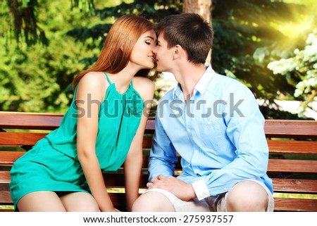 Young people tenderly kissing on a park bench. Love concept.