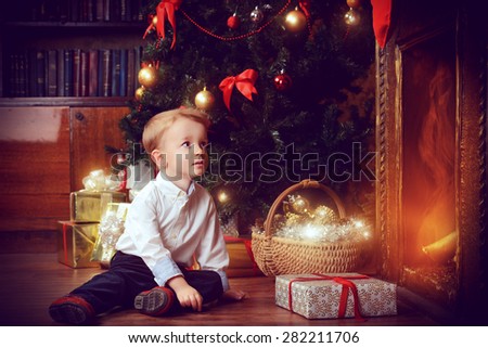 Cute little boy celebrating Christmas at home near the Christmas tree. X-mas decoration. Magic of the Christmas.