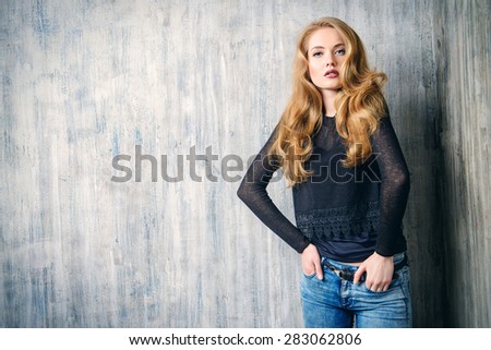 Beautiful blonde girl in jeans clothes posing by the grunge wall. Fashion.