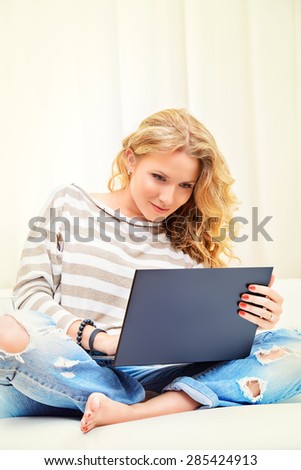 Smiling elegant woman sitting on a sofa with her laptop computer. Home interior, furniture. Lifestyle.