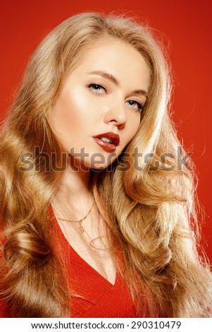 Charming smiling young woman in red dress and with blonde curled hair. Beauty, fashion. Cosmetics, make-up. Red background.