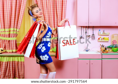 Fashionable pin-up girl standing with shopping bags on a pink kitchen. Retro style. Sale.