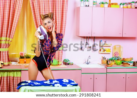 Charming pin-up girl ironing her dress and singing on a glamorous pink kitchen. Retro style. Fashion.