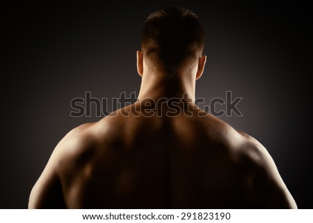 Athlete bodybuilder man demonstrating his perfect muscular body - muscles of the back and arms. Over black background.